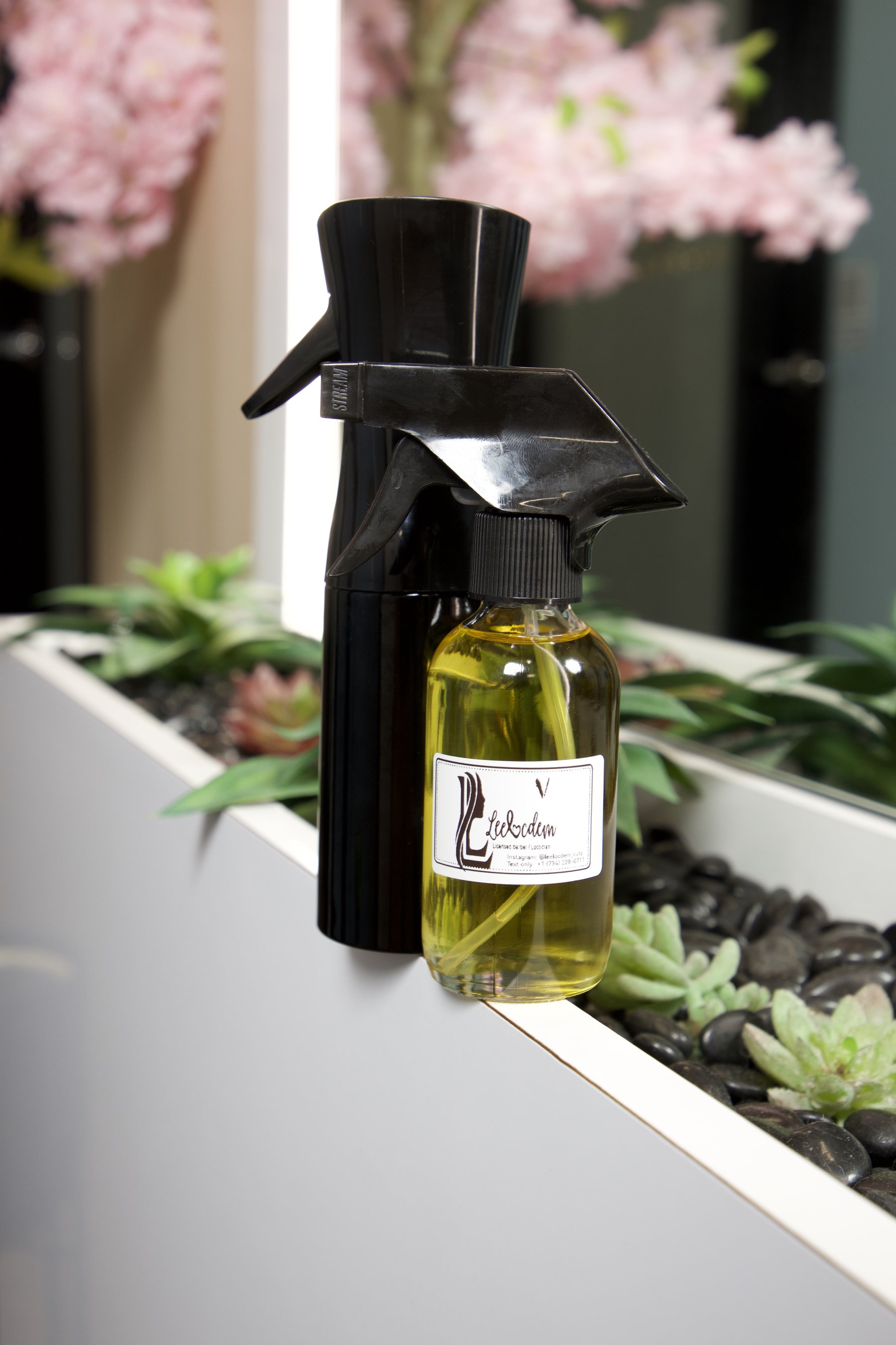 LEELOCDEM-branded hair oil and spray bottle on the studio planter